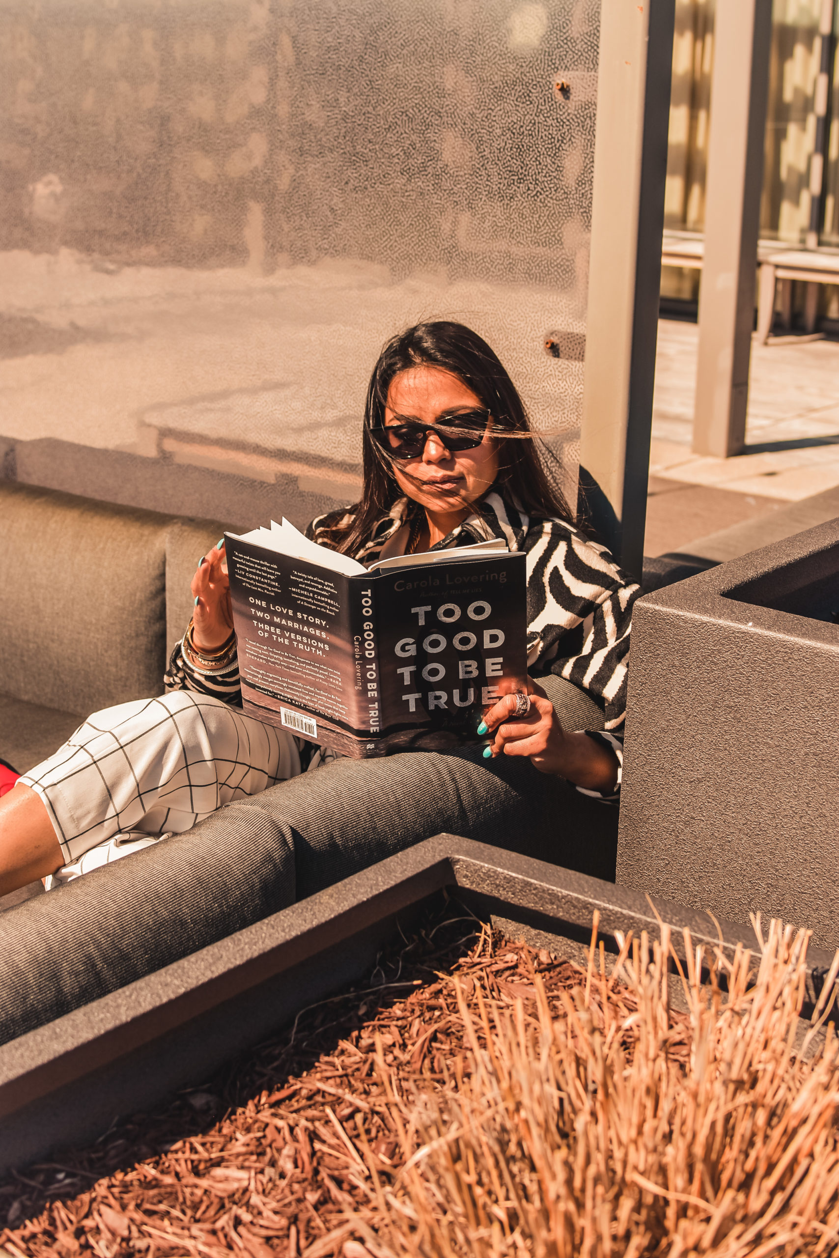 how to get back into reading. I am sitting on my rooftop terrace. I am wearing a zebra print shirt, plaid pants and red cowboy boots. I am reading a book called too good to be true. Myriad Musings, Saumya Shiohare 