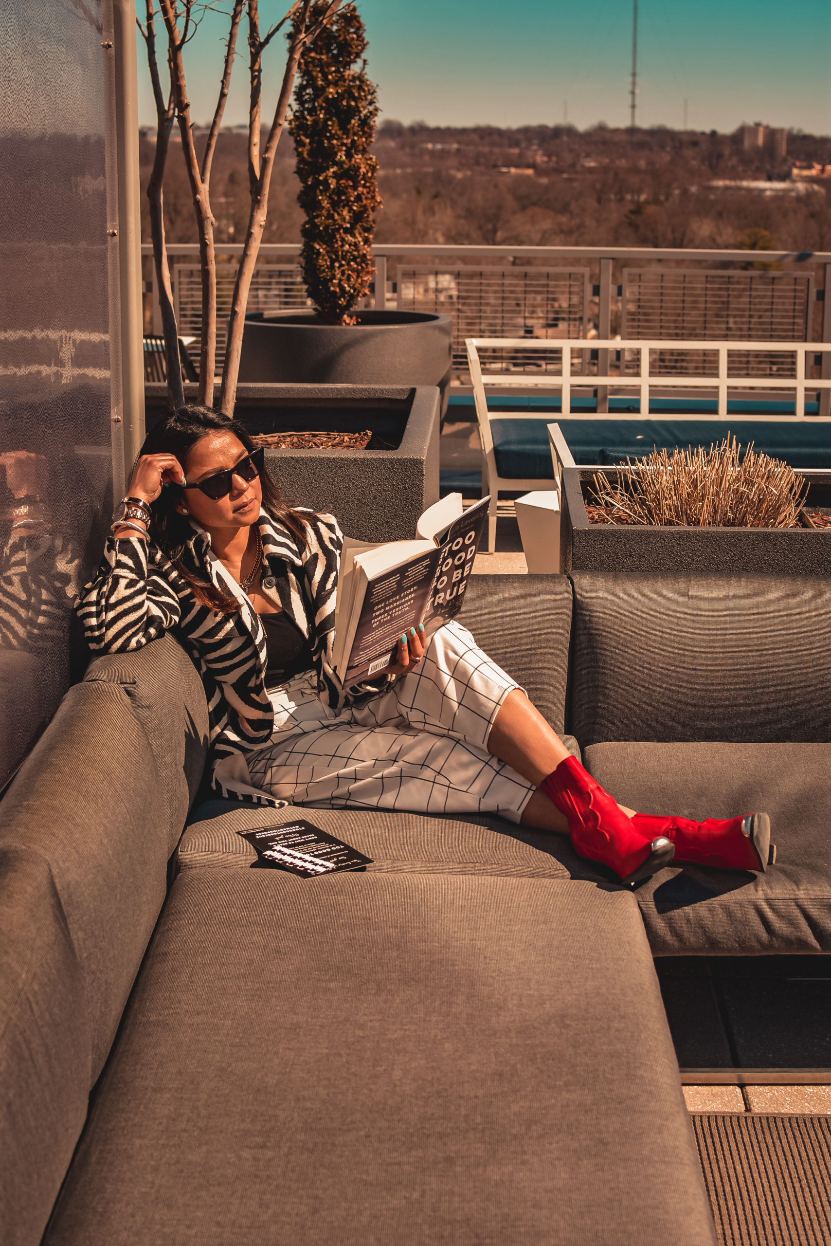 how to get back into reading. I am sitting on my rooftop terrace. I am wearing a zebra print shirt, plaid pants and red cowboy boots. I am reading a book called too good to be true. Myriad Musings, Saumya Shiohare 